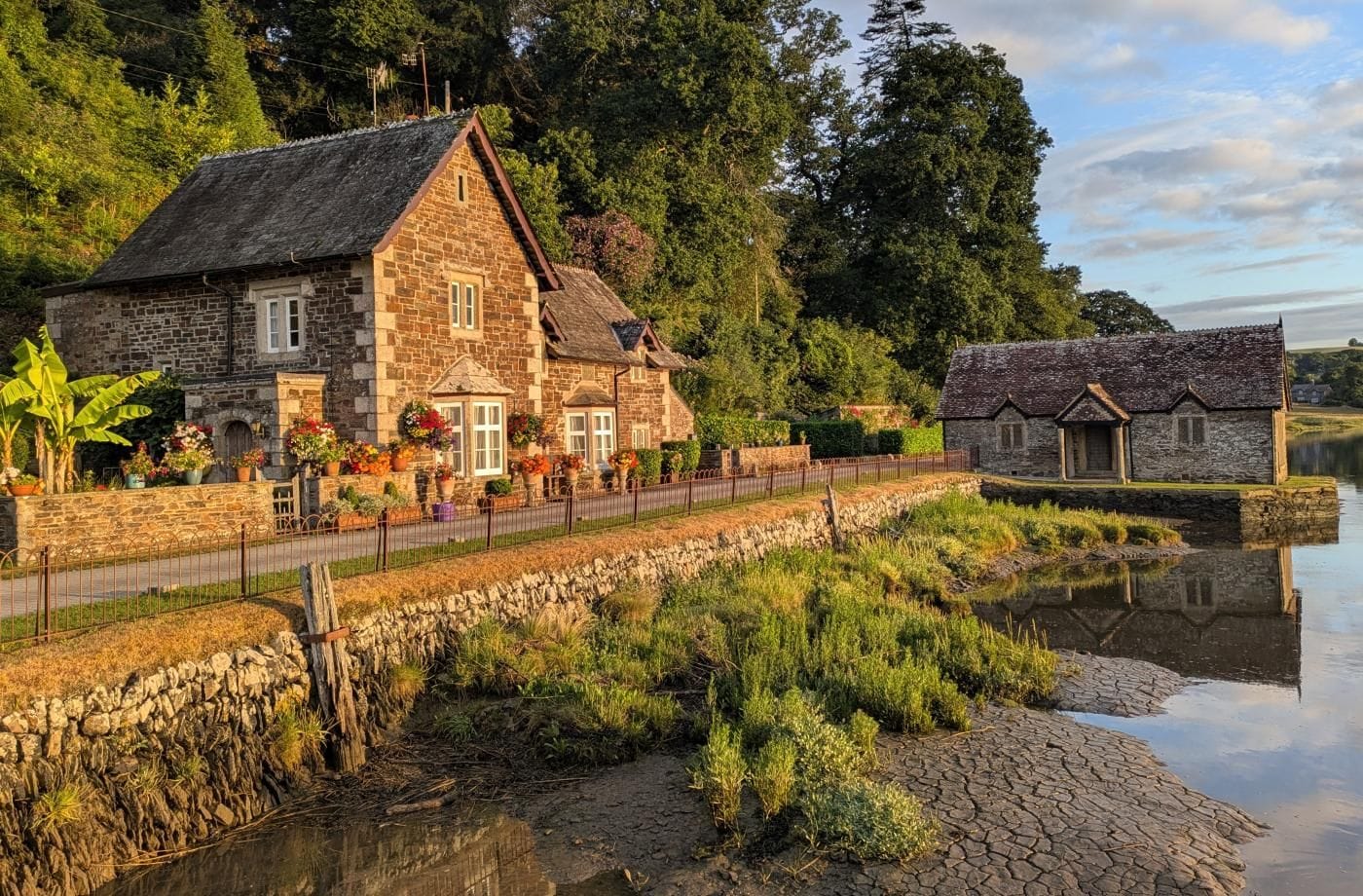 A stone house with a thatched roof, a stone wall, and a canal in front.