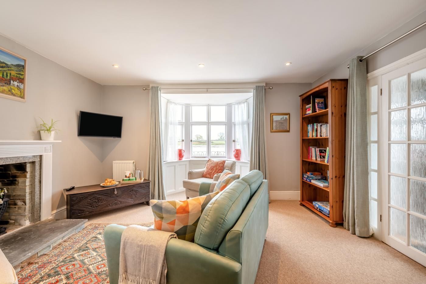 A living room with a fireplace, a sofa, a coffee table, a bookshelf, and a large window.