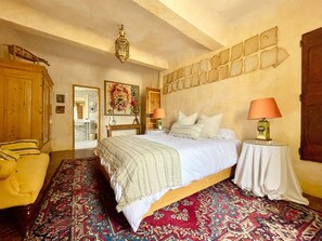 A bedroom with a bed, two bedside tables, a chair, a wardrobe, and a patterned carpet. - La Maison des Chapitres (FORCALQUIER)