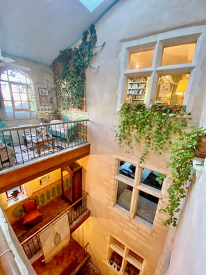 Un interior de varios niveles con un balcón, una escalera y una biblioteca.