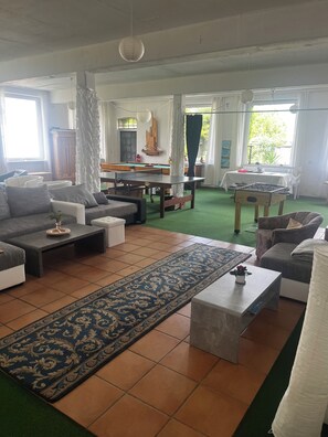 Ein Wohnzimmer mit einer Sofagarnitur, einem Couchtisch, einem Billardtisch und einem Kicker.