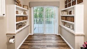 Un couloir doté d’un plancher en bois, d’étagères blanches ornées de paniers et d’objets décoratifs, d’une porte donnant sur l’extérieur et d’un porte-rouleau de papier toilette sur le côté gauche.