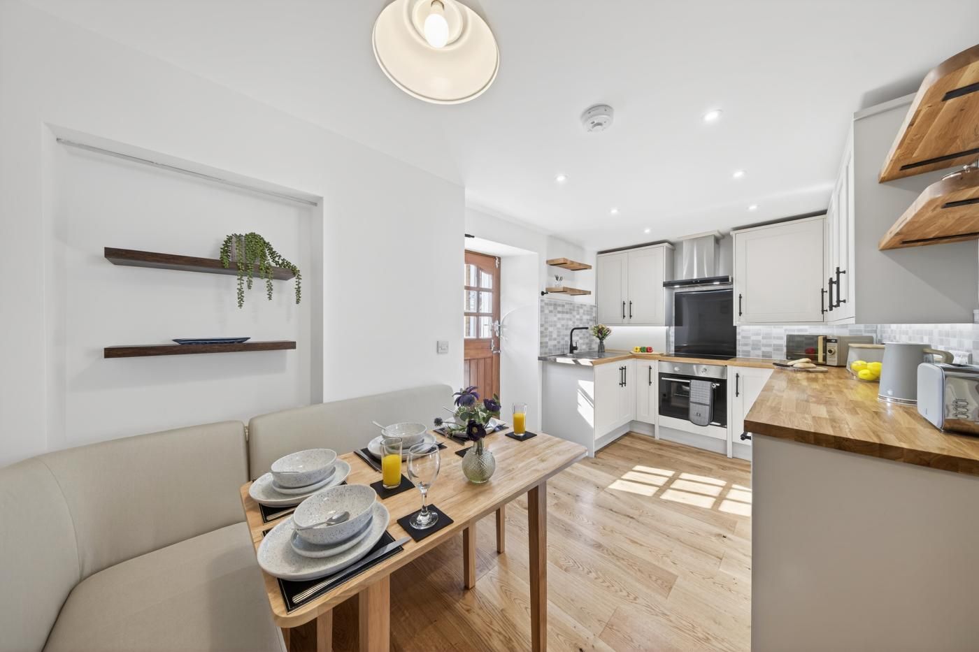A modern kitchen with white cabinetry, a wooden countertop, and a dining area with a table set for two.