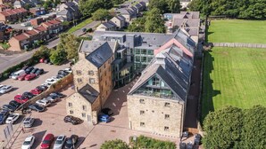 An aerial view of a modern building with a parking lot, surrounded by residential houses and greenery. - 2 Bed in Alnwick (oc-coq92) (Alnwick)