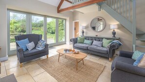 A spacious living room with a large window, a staircase, and a cozy seating area. - 2 Bed in Christon Bank (oc-coq128) (Christon Bank)