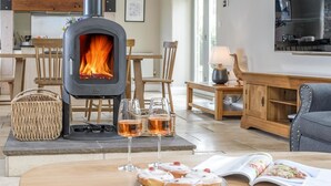 A cozy living room with a wood-burning stove, a dining table with pastries and glasses, and a comfortable seating area. - 2 Bed in Christon Bank (oc-coq128) (Christon Bank)
