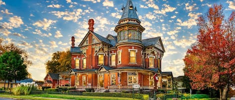 A large, historic house with multiple stories, a prominent turret, and a well-maintained front yard.