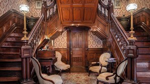 Una imponente escalera con trabajos de madera ornamentados y detalles en latón, que conduce a una puerta con la leyenda 'Patio'.