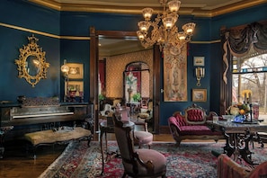 Una habitación con un piano de cola, muebles ornamentados, un candelabro y un espejo grande.