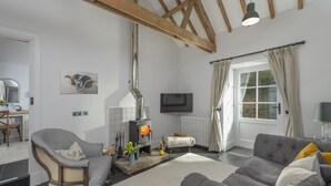 Ein Wohnzimmer mit Kamin, einer Couch, einem Sessel, einem Fernseher und einem Fenster mit Vorhängen.