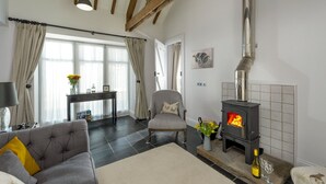 Ein Wohnzimmer mit Kamin, einer Couch, einem Sessel, einem Tisch mit Blumenvase und einem Fenster mit Vorhängen.