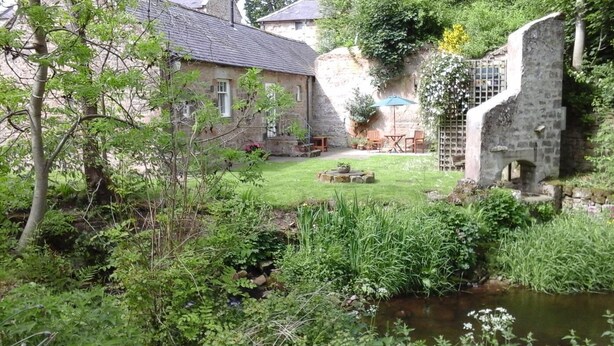 Ein Steinhaus mit Garten, einem kleinen Teich und einer Steinsäule.