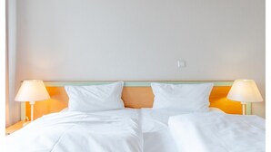 Een hotelkamer met een tweepersoonsbed, twee bedlampjes en een effen muur.