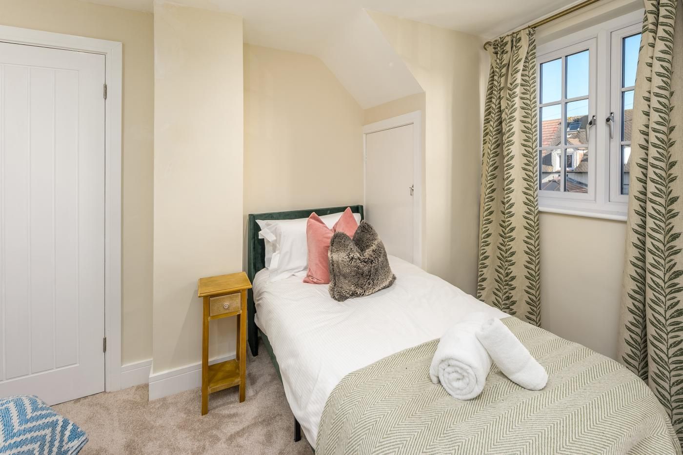 A bedroom with a bed, a nightstand, a window with curtains, and a door.