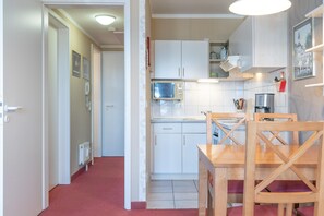 A compact kitchen with white cabinets, a microwave, and a dining table with wooden chairs. - Perfekt fur Familien - Ferienwohnung mit Balkon in Sellin (Sellin)