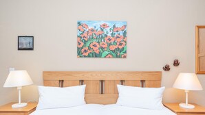 Una camera d'albergo con una testiera in legno, biancheria da letto bianca, due lampade da comodino e un quadro con fiori al muro.
