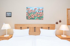 A hotel room with a wooden headboard, white bedding, two bedside lamps, and a painting of flowers on the wall. - Perfekt fur Familien - Ferienwohnung mit Balkon in Sellin (Sellin)