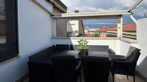 Eine Dachterrasse mit Tisch und Stühlen, einem Blumentopf und Blick auf Gebäude und Berge.