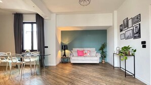 Ein modernes Wohnzimmer mit einer Couch, einem Esstisch mit Stühlen, einem Couchtisch, einer Lampe und einer Pflanze.
