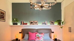Ein Schlafzimmer mit einem Bett, zwei Nachttischen, einer Chandelüster, einem Regal mit Büchern und gerahmten Bildern sowie einem Kleiderschrank.