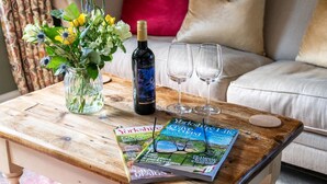 Ett träbord med en vinflaska, två glas, en tidning och en vas med blommor.