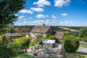 A stone house with a hot tub and outdoor seating area, surrounded by lush greenery and a scenic countryside view. - 4 Bed in Norwood (oc-b35549) (Norwood)