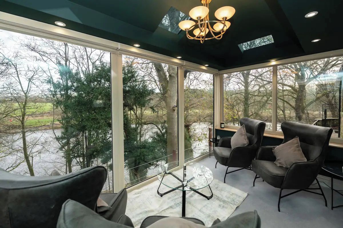 A modern room with large windows, a chandelier, and two leather armchairs.