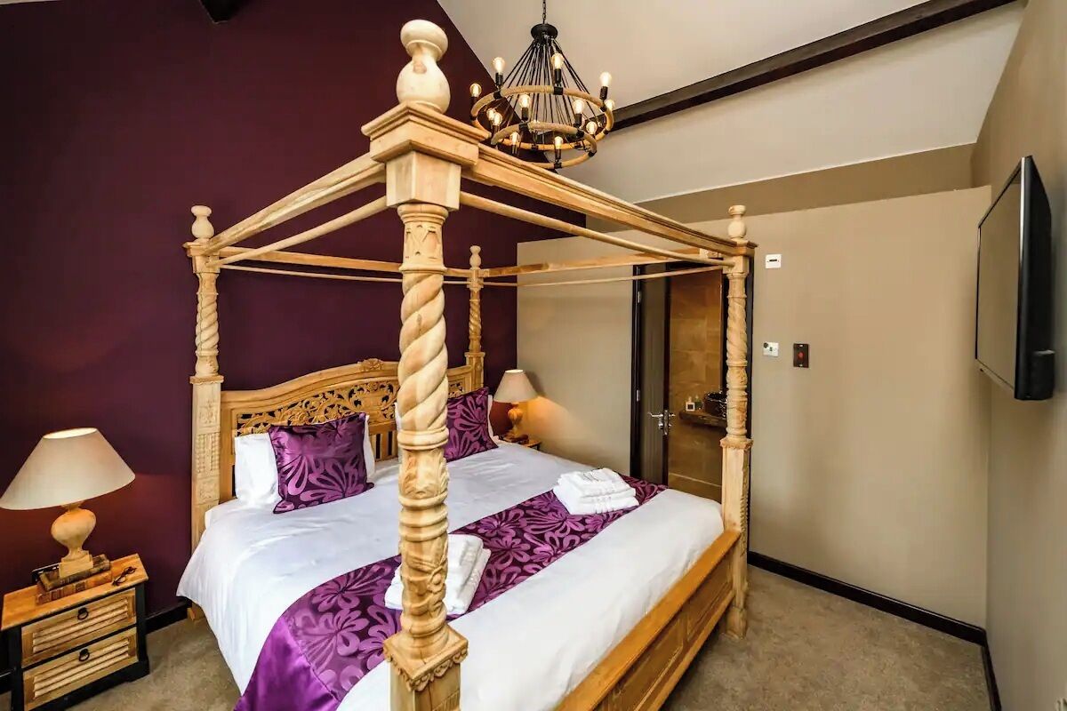 A four-poster bed with a chandelier, a bedside table with a lamp, and a mirror on the wall.