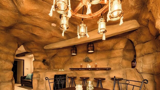 Un interior rústico con pared de piedra, vigas de madera en el techo y una mesa redonda con sillas.