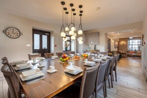 A dining area with a wooden table set for a meal, surrounded by chairs. A fruit bowl is on the table, and there is a clock on the wall. - 7 Bed in Kendal (oc-t36284) (Kendal)