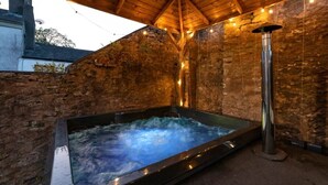 Un jacuzzi en un entorno exterior con un muro de piedra de fondo y una estructura de techo de madera.