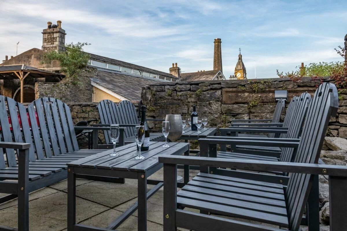Outdoor seating with tables and chairs, a stone wall, and a clock tower in the background.