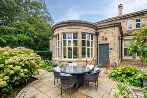 A stone building with a round corner, a glass conservatory, and a patio with wicker furniture. - 2 Bed in Crook O Lune (oc-r36290) (Halton)
