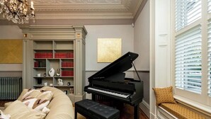 Um piano de cauda numa sala com estante, radiador e janela com persianas.
