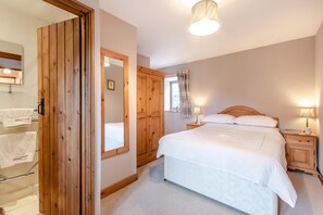 A bedroom with a bed, wooden wardrobe, a mirror, a bedside table with a lamp, and a window with curtains. - 2 Bed in Thwaite (oc-s36623) (Thwaite)