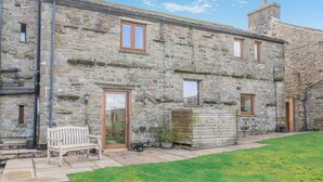 A stone building with a wooden bench, a door, and a small garden area. - 2 Bed in Thwaite (oc-s36623) (Thwaite)