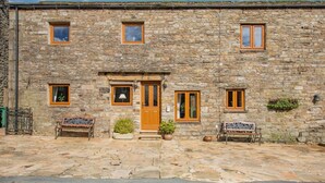 A stone building with a wooden door, multiple windows, and outdoor seating. - 2 Bed in Thwaite (oc-s36623) (Thwaite)