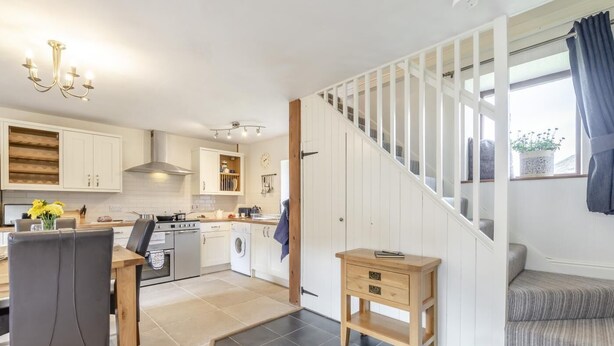 A modern kitchen with a dining area, a staircase, and a small wooden side table. - 2 Bed in Thwaite (oc-s36623) (Thwaite)