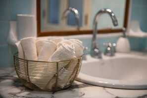 A bathroom with a marble countertop, a white sink, a gold-rimmed basket with white towels, and a mirror reflecting a faucet and a toilet. - Corso View Apartment (Cagliari)