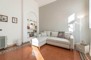 A modern living room with a sectional sofa, a radiator, a bookshelf, and a lamp. - Corso View Apartment (Cagliari)
