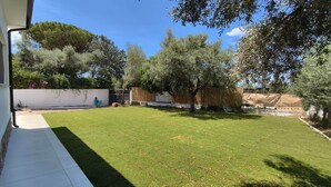 Un jardin avec une pelouse, des arbres, un mur blanc et une clôture en bois.