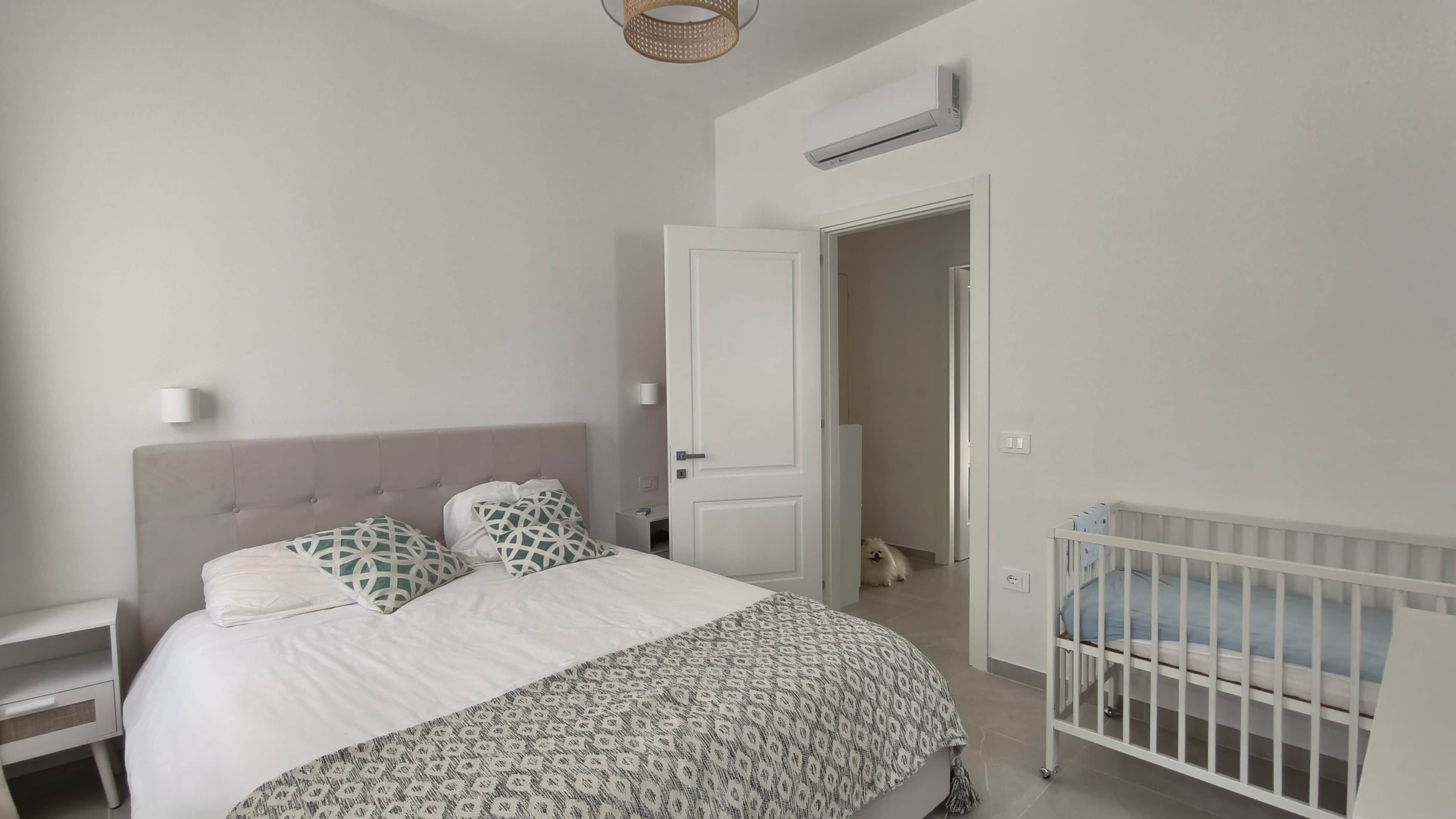 Une chambre à coucher comprenant un lit, une table de chevet, un berceau, une porte et un appareil de climatisation.