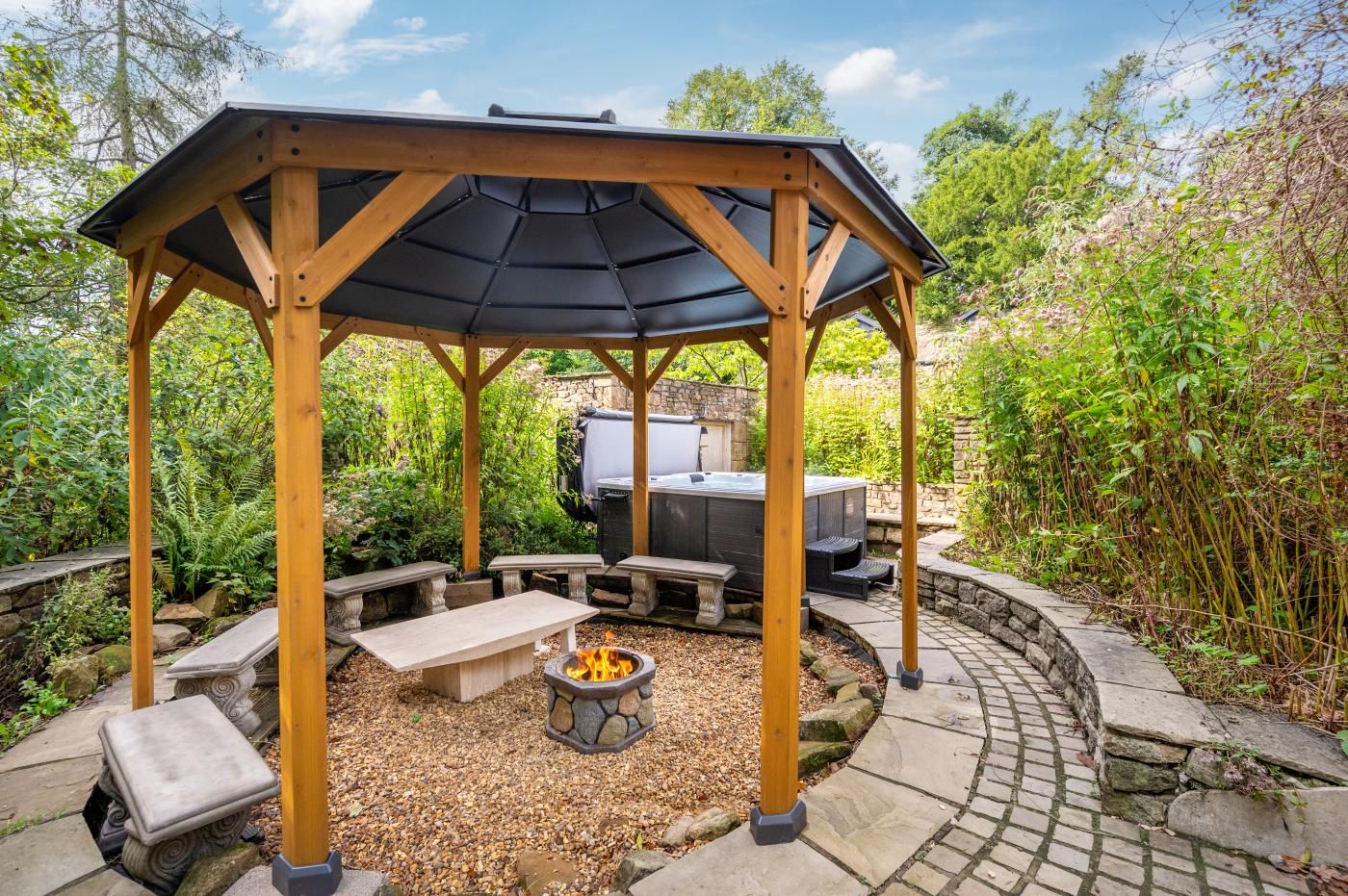 A covered outdoor seating area with a fire pit, stone benches, and a grill.