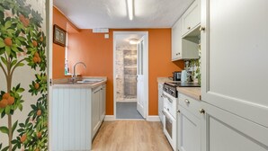 A compact kitchen with a sink, stove, and cabinets, leading to a hallway with a door. - 2 Bed in Appledore (oc-j36297) (Appledore)