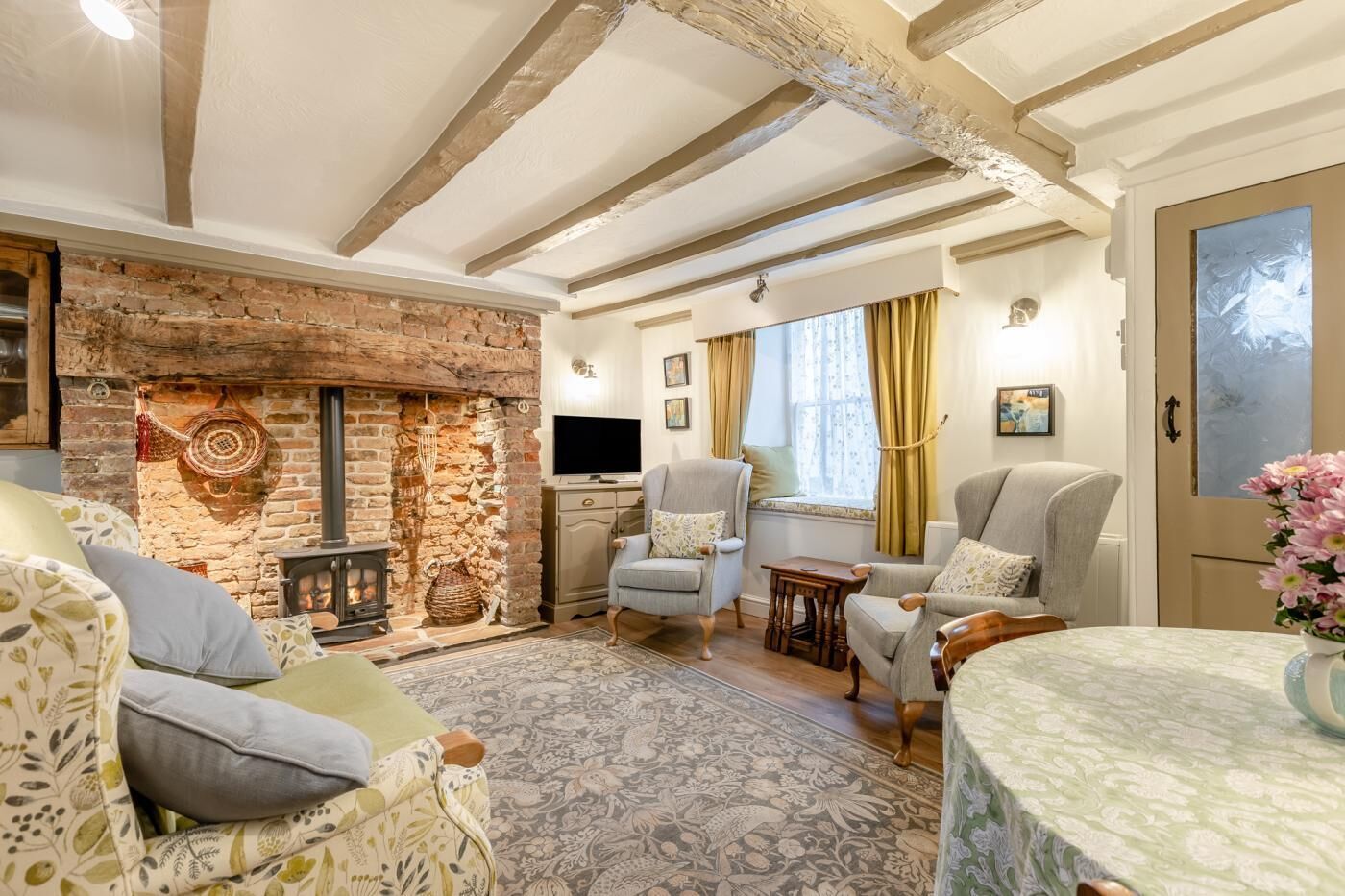 A cozy living room with exposed wooden beams, a stone fireplace, comfortable seating, and a television.