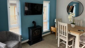 A room with a blue wall, a flat-screen TV, a fireplace, a dining table with chairs, and a mirror. - 2 Bed in Troutbeck Bridge (oc-p36885) (Troutbeck Bridge)