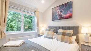 Ett hotellrum med en säng, två sänglampor, ett fönster med gardiner, ett element och en tavla på väggen.