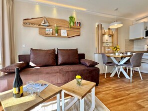 A modern living room with a brown sofa, wooden coffee table, and a dining area with a white table and chairs. - Ferienwohnung in Sellin mit Balkon in Sudostlage (Sellin)