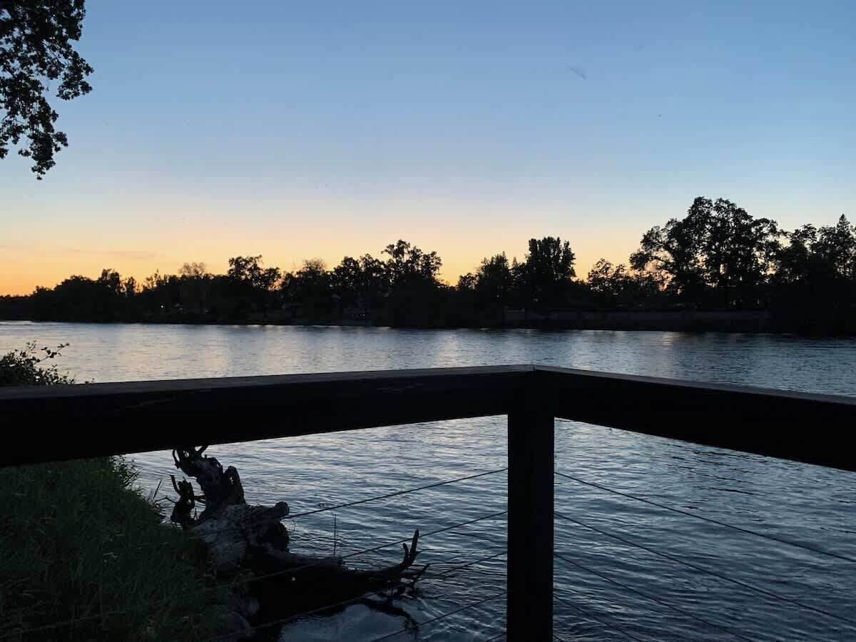 Ein Fluss bei Sonnenuntergang, im Vordergrund eine Holzbrüstung.