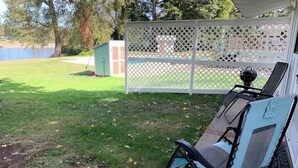 A patio with two lounge chairs, a grill, and a white lattice fence.
